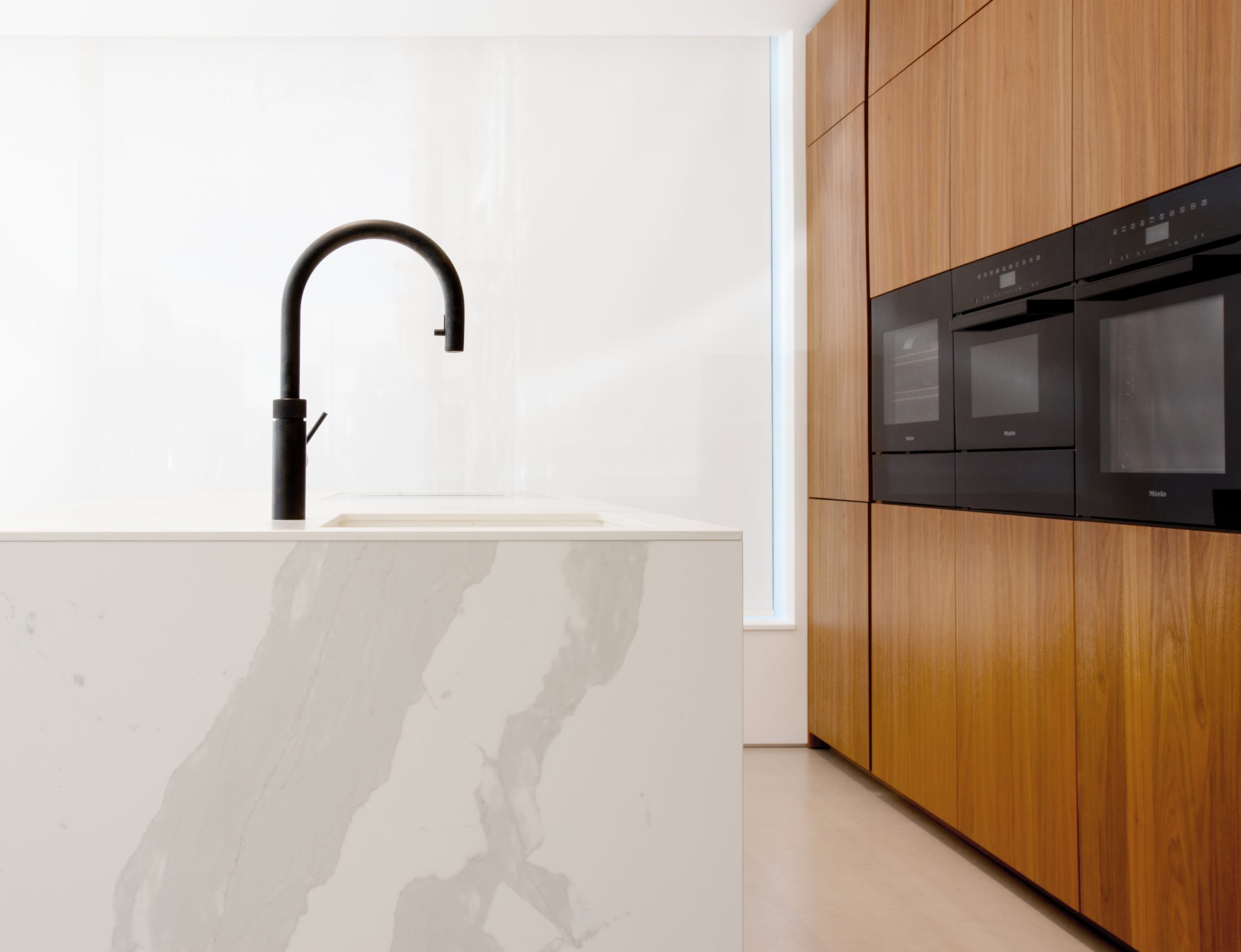 Built-in Miele kitchen appliances and a marble-effect island with matte black tap, from the Studio & Build showroom